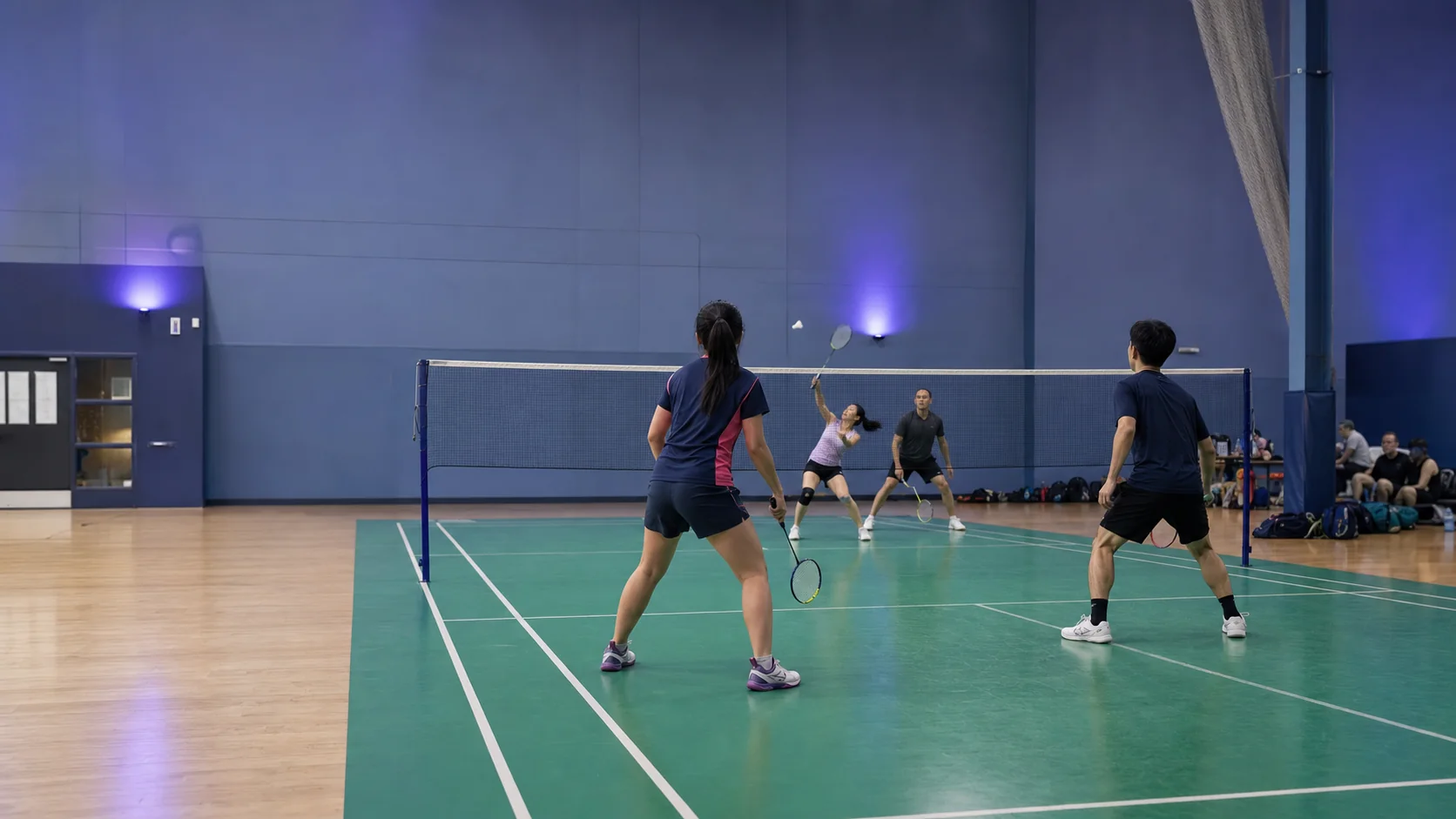 Four amateur players playing doubles badminton in a community sports hall